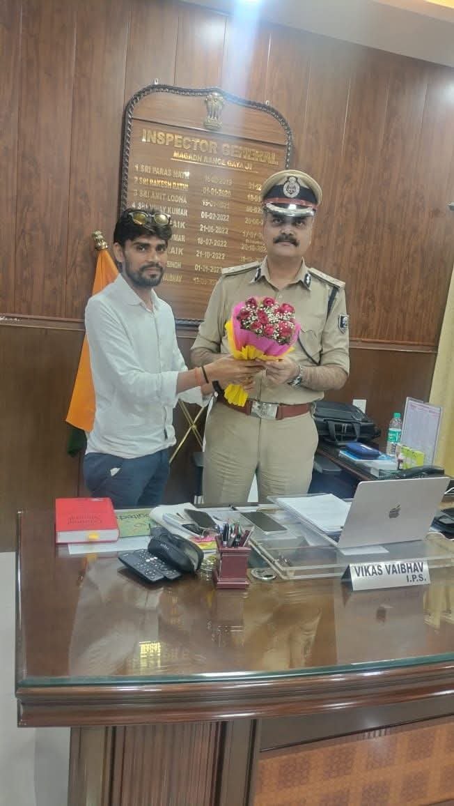 A man presenting a bouquet of flowers to a senior police officer in uniform across an office desk