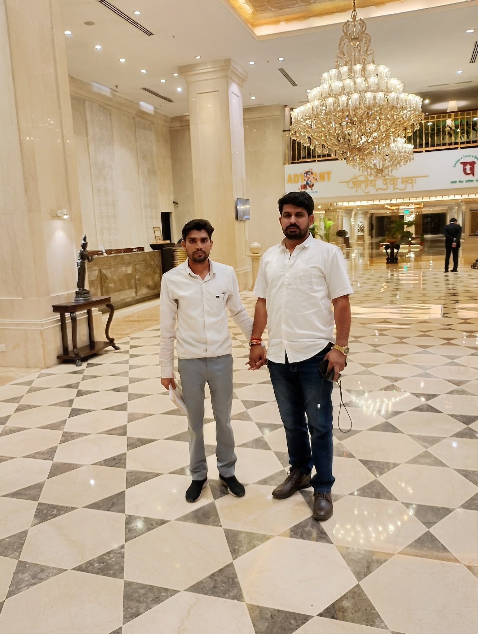 Two men standing in a large banquet hall lobby with a chandelier overhead