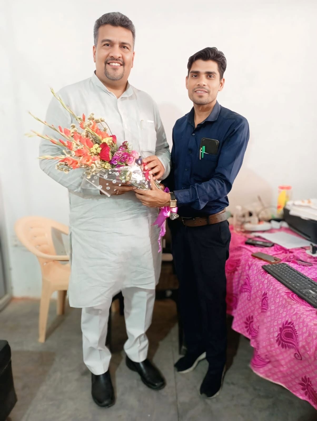 A man presenting a bouquet of flowers to another man in a small office